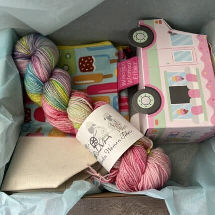 A packaged woolen creamery order including a yarn truck with goodies inside, brightly colored skein of yarn, and a popsicle project bag and sundae charms.