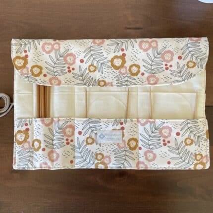 A partially open knitting needle roll with exterior floral print and a cream colored lining visible. There are various wooden needles in the slots.