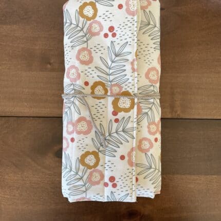 A folded open knitting needle roll with exterior floral print secured with a beige cotton cord.