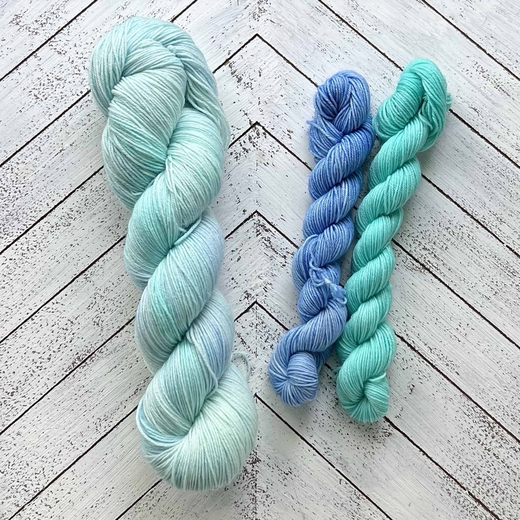 A large skein of pale blue yarn and two small skeins of blue and aqua yarn.