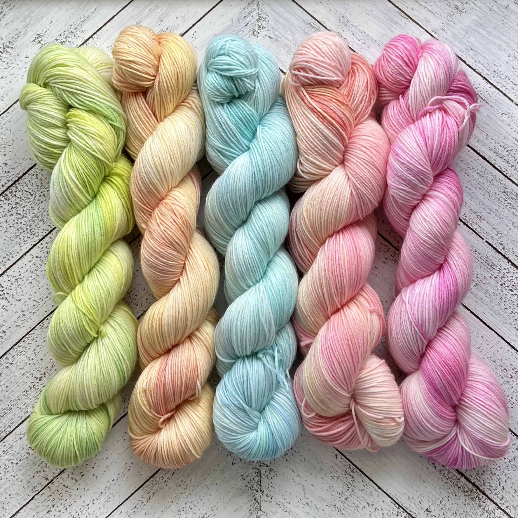 Five skeins of yarn in pastel green, yellow, blue, peach and pink.
