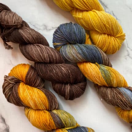 Four skeins of yarn laid out in yellow with browns and grays.