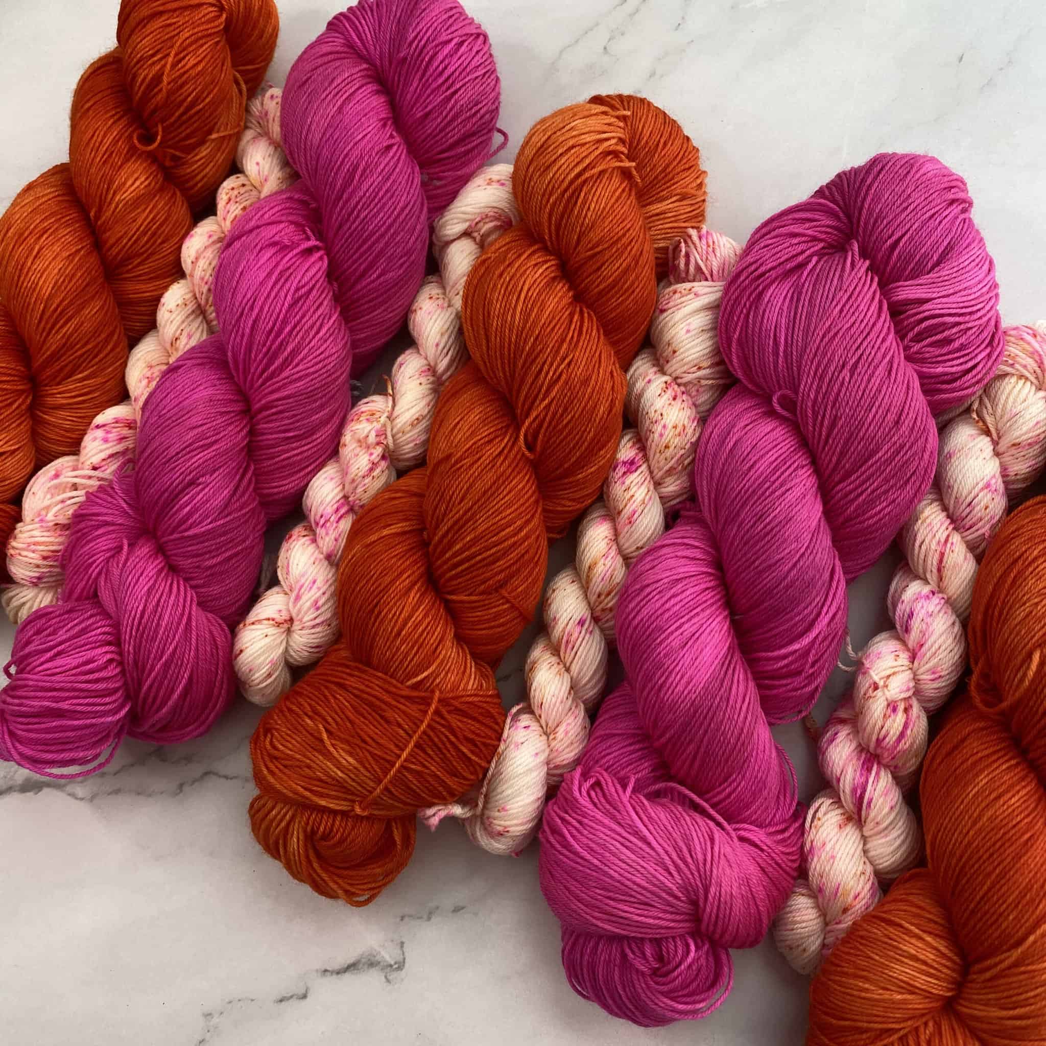 Skeins of hot pink and orange yarn with small, speckled mini skeins in between.