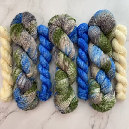 Skeins of blue, green and cream yarn with small mini skeins of blue and cream in between.