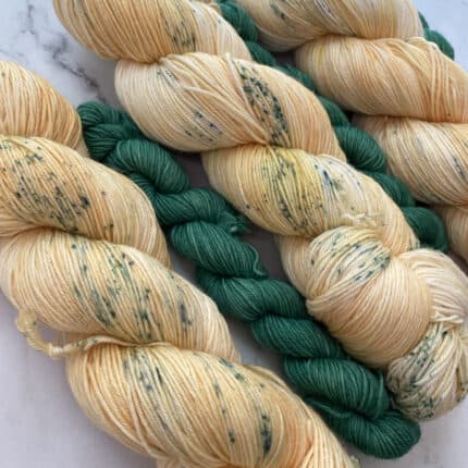 Cream-colored skeins of yarn with green speckles, with small skeins of green yarn in between.