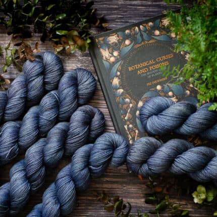 Six skeins of blue-purple yarn surrounded by ferns and a book with the title Botanical curses and poisons.