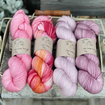 Four skeins of yarn in shades of pink and purple.
