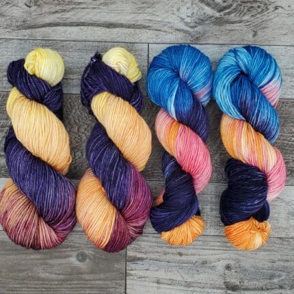 Four skeins of variegated yarn that transition from deep purples to warmer colors in lighter shades.