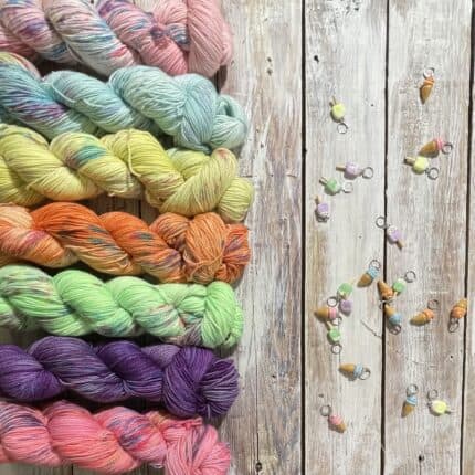 Skeins of bright pink, blue, yellow, orange, green, purple and pink yarn next to ice cream cone stitch markers.