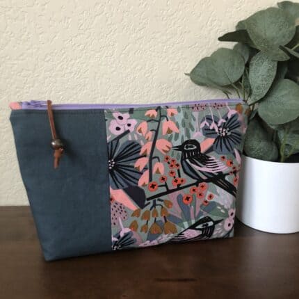 A zipper pouch featuring a floral fabric print with a bird and an accent fabric of teal color.
