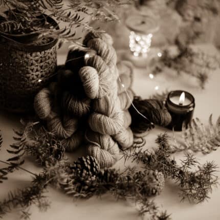 Skeins of yarn surrounded by dry leaves, a candle and a metal vase, in black and white.