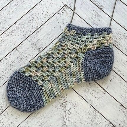 A crocheted sock in blues and greens.