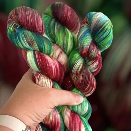 A light-skinned hand holding three skeins of red and green variegated yarn.