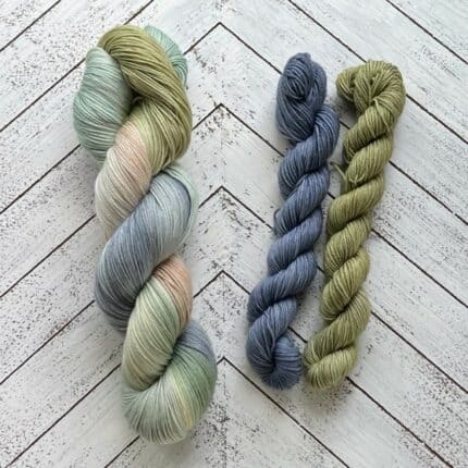 A large skein of yarn in blues and greens and two small skeins in blue and green.