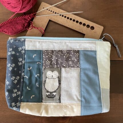 A quilted patchwork zipper pouch in cream and blue tones featuring a sleepy owl.