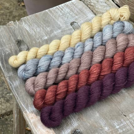 Five mini skeins of yarn. From top to bottom the colours are beige, blue with speckles, lich briwn, reddish brown and purple.
