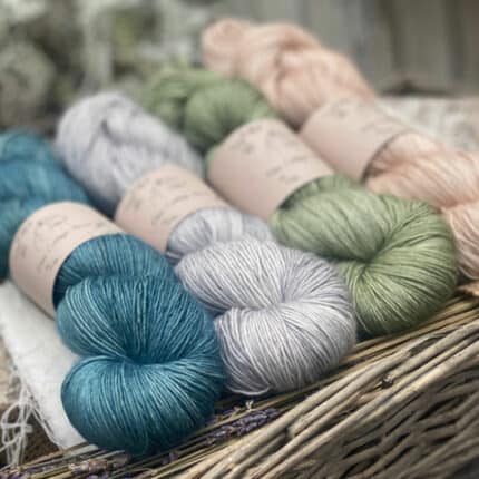Four skeins of yarn. From left to right the colours are blue, grey, green and beige.