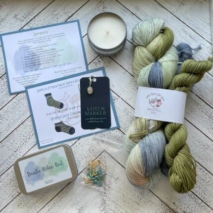 Yarn in blues and greens, small candle, stitch markers, notion tin and card insert.