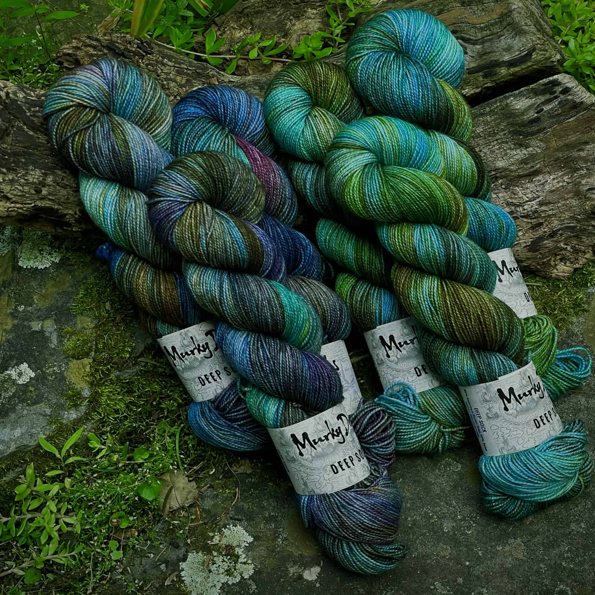 A group of two different multicolored yarns in golds, greens and blues.