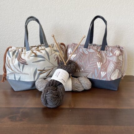 A collection of two canvas project bags in blue, gray and taupe floral fabric with drawstring closures.