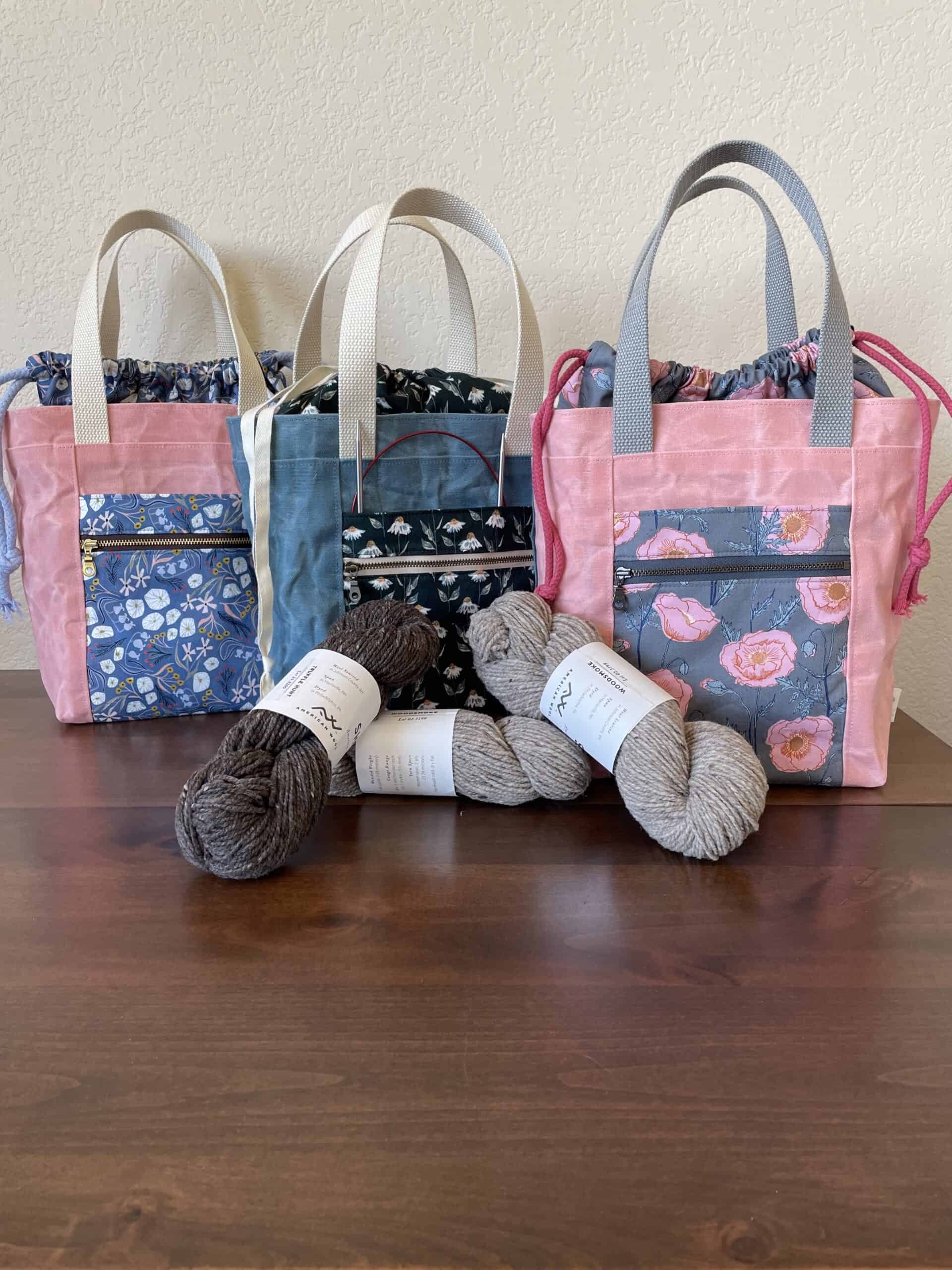 A collection of three waxed canvas project totes in pink and blue floral fabric with drawstring closures.