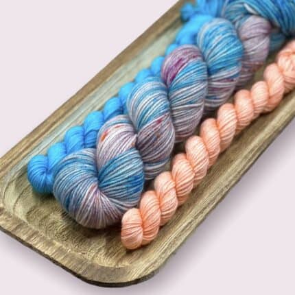 A full sized skein and two mini skeins of blue and pink yarn.