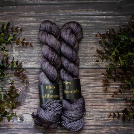 Two lilac skeins on a wood background surrounded by plants.