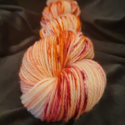 A skein of worsted weight yarn in shades on pinks and oranges on a cream background.