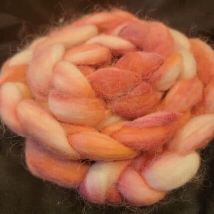 A bundle of alpaca spinning fiber in shades on pinks and oranges on a cream background.