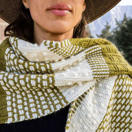 A closeup of a white and olive shawl around a woman’s neck, featuring a variety of textured stitch patterns.