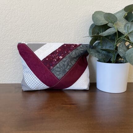 A quilted patchwork zipper pouch in ruby and white tones.