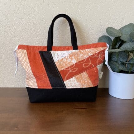 A quilted patchwork bag in orange and black tones featuring a drawstring closure.
