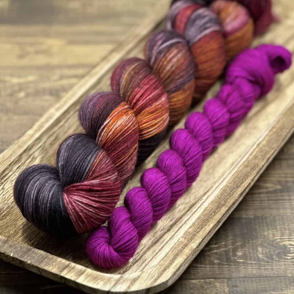 A skein of variegated pinks/purples/oranges yarn with a pink mini skein.
