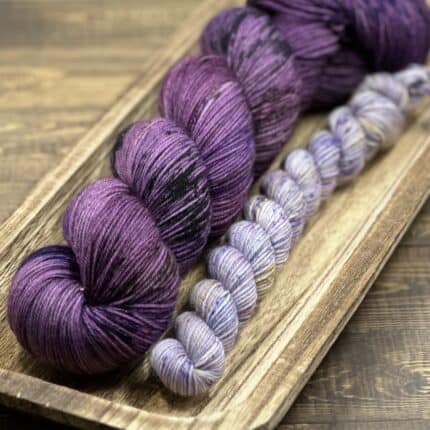 A skein of variegated purple yarn with a lavender mini skein.