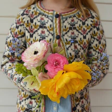 A young child in a floral sweater holding a bouquet.