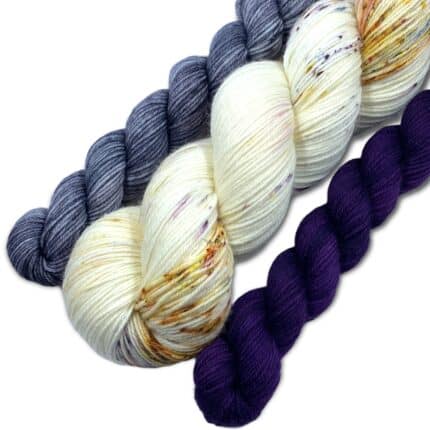 A large hank of cream yarn with two mini skeins of yarn in gray and purple.