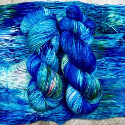 Two mostly blue skeins of fingering weight yarn, with some small areas of white and green.