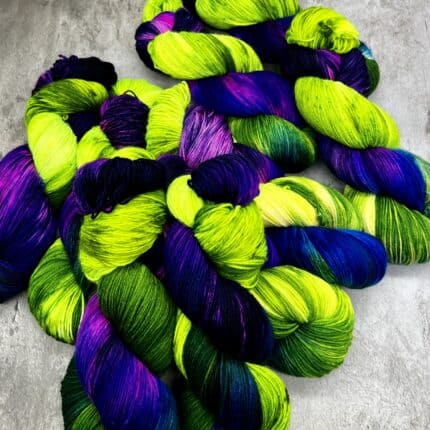 A pile of skeins in neon green, purple and brilliant blue on a grey backdrop.