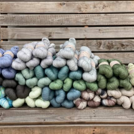 A pile of skeins of Brimham Bio Fingering yarn in shades of blues, greens, greys and browns.