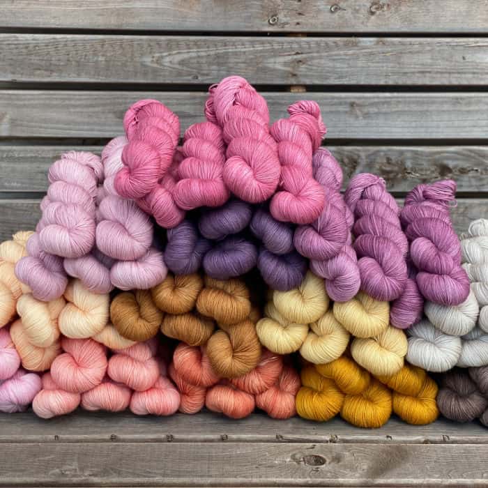 A pile of skeins of Brimham Bio Fingering yarn in shades of pinks, purples, yellows and browns.