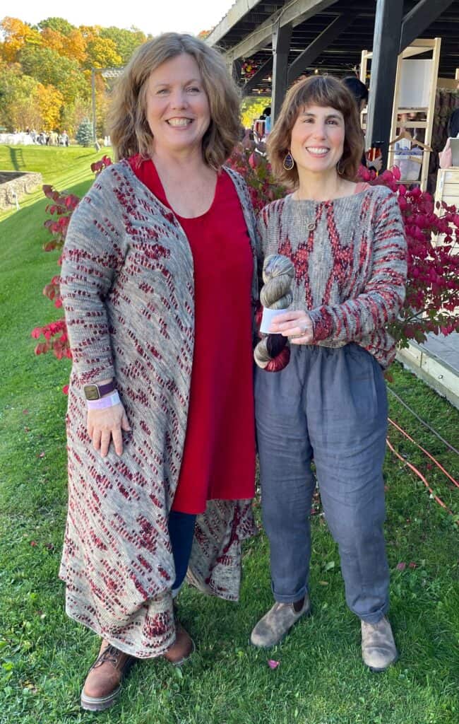 wo light-skinned women, one wearing a long cardigan and the other a pullover in gray-blue yarn with red-purple bobbles.