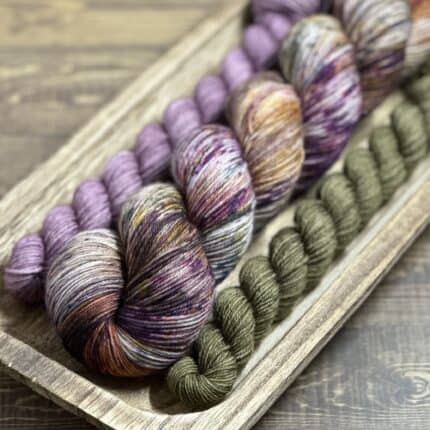 A large skein of variegated blue, purple and orange yarn with a mini skein of lavender and a mini skein of mossy green.