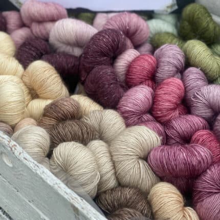 A box of skeins of yarn in shades of purple, pink, beige, brown and green.