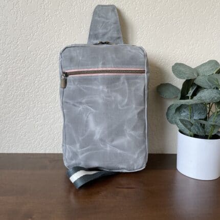 A grey waxed canvas sling bag with pink zips.