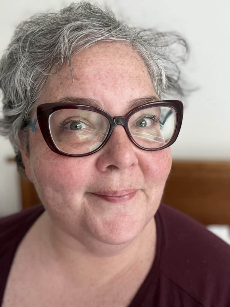 A light-skinned woman with gray hair wearing brown glasses.