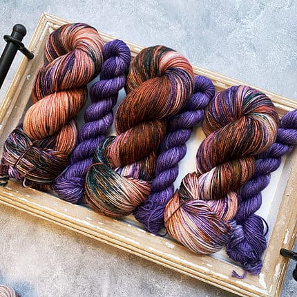 Full skeins of yarn in brown and purple paired with deep purple mini skeins.