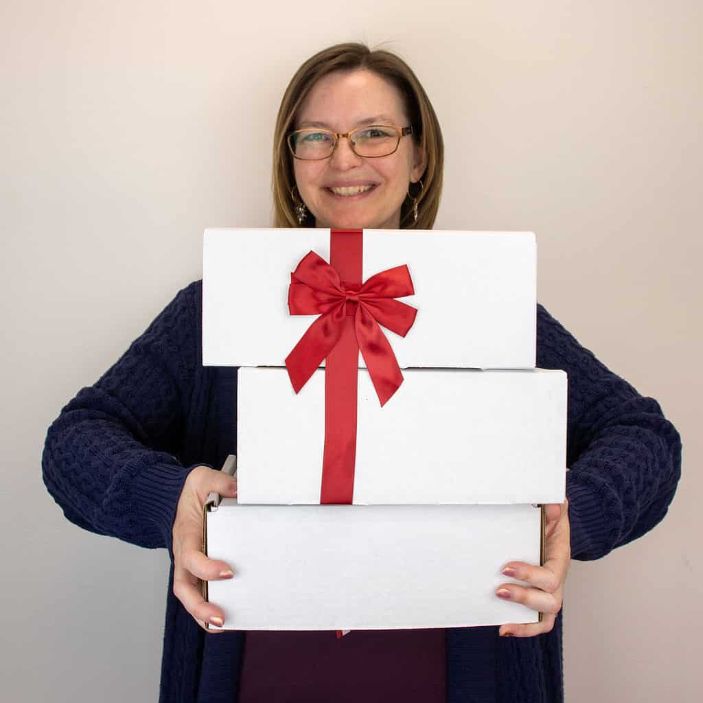 A light-skinned woman holding three white boxes with a big red bow.
