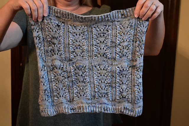 A light blue speckled lace cowl held up by light-skinned hands. 