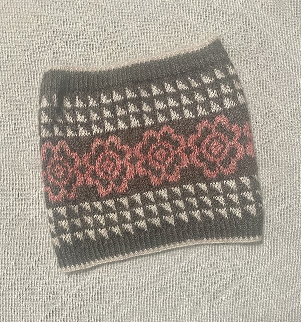 A gray colorwork cowl with pink flowers and white triangles.
