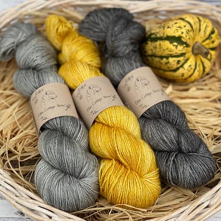 Three skeins of yarn in shades of grey and yellow.